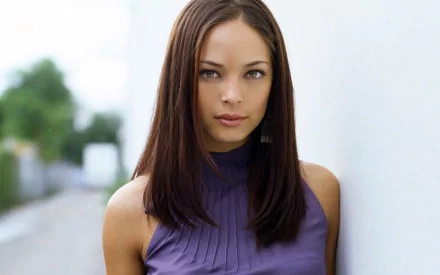 A high-definition desktop wallpaper featuring celebrity Kristin Kreuk, showcasing her with long brown hair and a purple top against a blurred background.