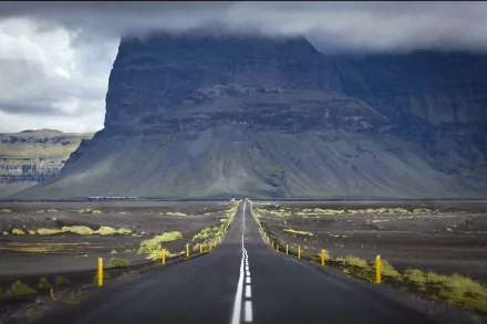 A striking HD desktop wallpaper features a long, straight road leading towards a dramatic mountain landscape under a cloudy sky, emphasizing the beauty of man-made paths in nature.