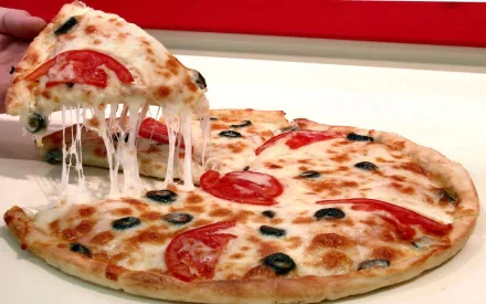 A delicious pizza topped with fresh tomatoes and black olives, featuring melted cheese pulling away, set against a vibrant background—an appealing HD desktop wallpaper for food lovers.