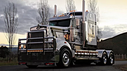 HD desktop wallpaper showcasing a powerful Kenworth truck parked with tall trees and a cloudy sky in the background.