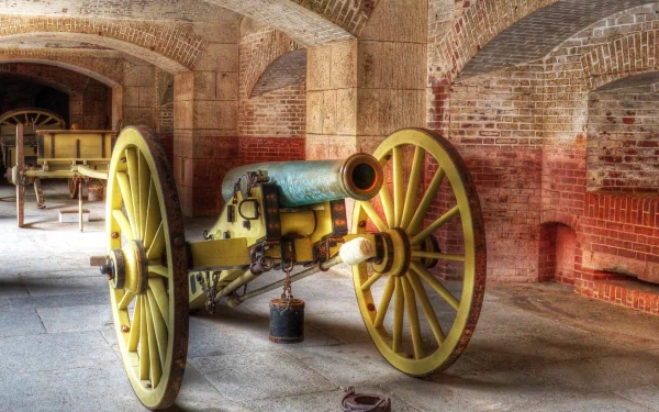HD PC desktop wallpaper of a historic military artillery cannon with large yellow wheels inside a brick-arched fort or storage room.
