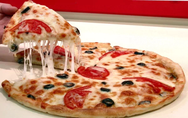 A delicious pizza topped with fresh tomatoes and black olives, featuring melted cheese pulling away, set against a vibrant background—an appealing HD desktop wallpaper for food lovers.