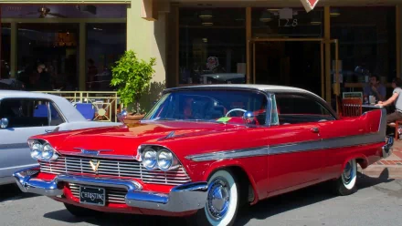 A striking 1958 Plymouth Fury in vivid red, parked outside a storefront, capturing the essence of classic American automotive design. This image serves as a stunning HD desktop wallpaper.