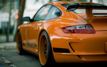 HD PC desktop wallpaper of an orange Porsche sports car, rear three-quarter view on a city street showcasing glossy curves and a prominent rear wing.