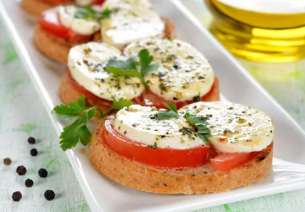 A visually appealing HD desktop wallpaper featuring fresh sandwich slices topped with tomato, mozzarella, and herbs, served on a white platter with a drizzle of olive oil.