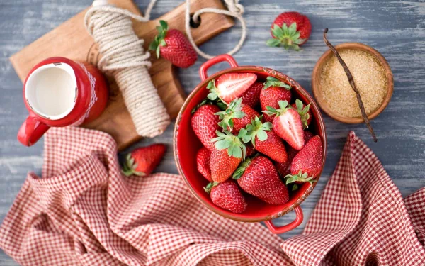 HD PC desktop wallpaper featuring fresh strawberries in a red pot, with a jug of cream, sugar bowl, and twine on a rustic wooden surface and checked cloth.