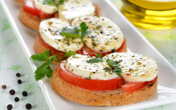 A visually appealing HD desktop wallpaper featuring fresh sandwich slices topped with tomato, mozzarella, and herbs, served on a white platter with a drizzle of olive oil.