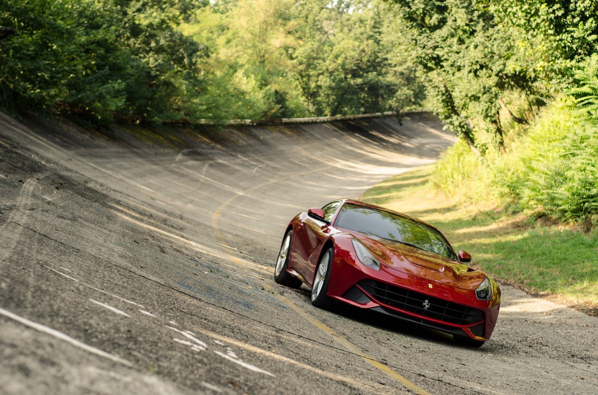 HD PC desktop wallpaper featuring a red Ferrari Berlinetta driving on a curved, vintage racetrack surrounded by lush green trees.