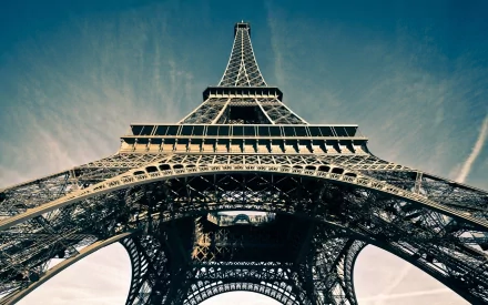 HD desktop wallpaper featuring a close-up, upward view of the Eiffel Tower against a clear blue sky, showcasing its intricate ironwork and majestic height. Man-made marvel in high resolution.