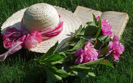 Still life photography of a straw hat with a pink ribbon, pink peonies, and an open book on green grass, captured in HD for a PC desktop wallpaper and background.