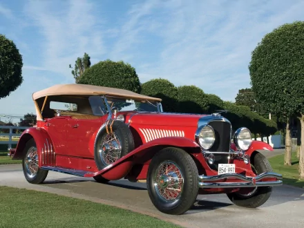 Vintage red Duesenberg Model J convertible parked outdoors under a blue sky, featured as an HD PC desktop wallpaper and background.