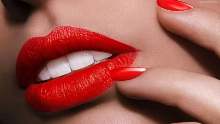 Close-up of a woman's lips adorned with striking red lipstick, complemented by manicured red nails, set against a smooth background as an HD desktop wallpaper.