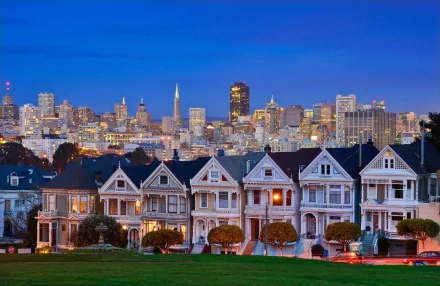 A stunning HD wallpaper featuring the Painted Ladies, iconic Victorian houses in San Francisco, with a vibrant city skyline at dusk in the background.