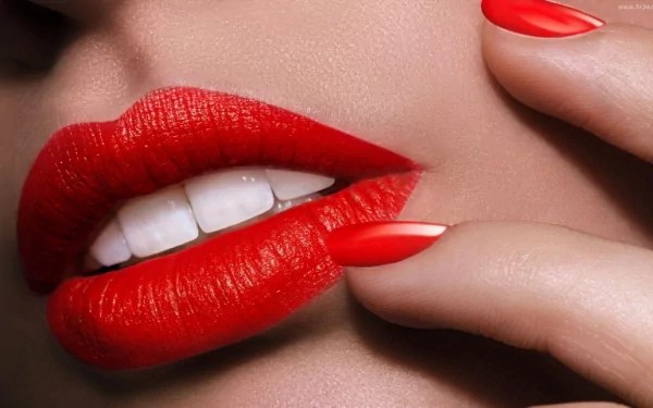 Close-up of a woman's lips adorned with striking red lipstick, complemented by manicured red nails, set against a smooth background as an HD desktop wallpaper.