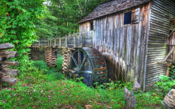 HD desktop wallpaper of a rustic man-made watermill surrounded by lush greenery and forest, capturing a serene and natural landscape.