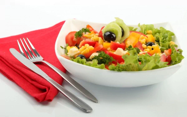 HD PC desktop wallpaper featuring a colorful fresh salad with lettuce, tomatoes, corn, olives, and peppers, accompanied by a fork and knife on a red napkin.