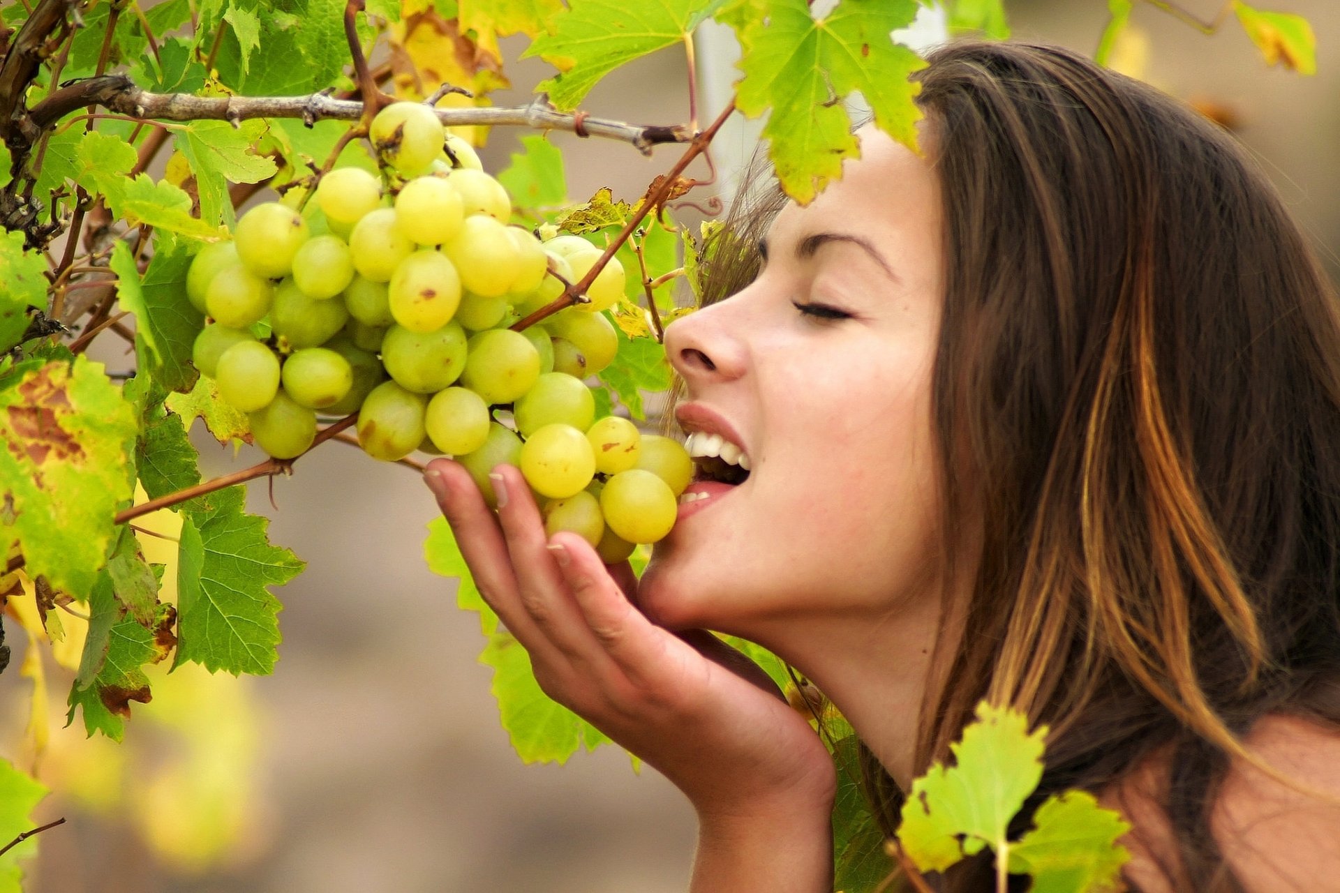 HD PC desktop wallpaper featuring a close-up of a woman model gently holding and admiring a bunch of green grapes amidst leafy vines.