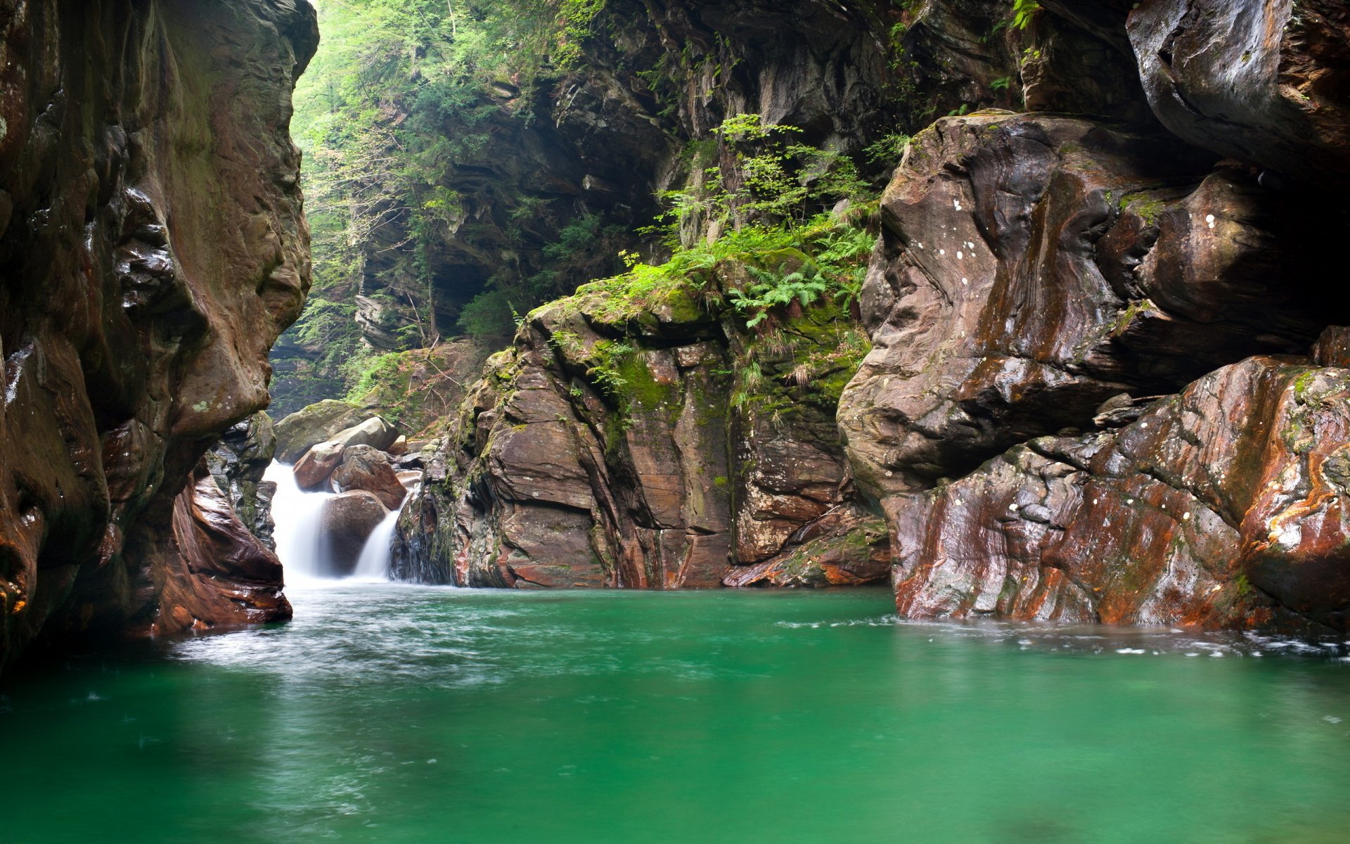 HD PC desktop wallpaper featuring a serene nature scene with a turquoise river flowing through a rocky cliff gorge surrounded by lush green foliage.