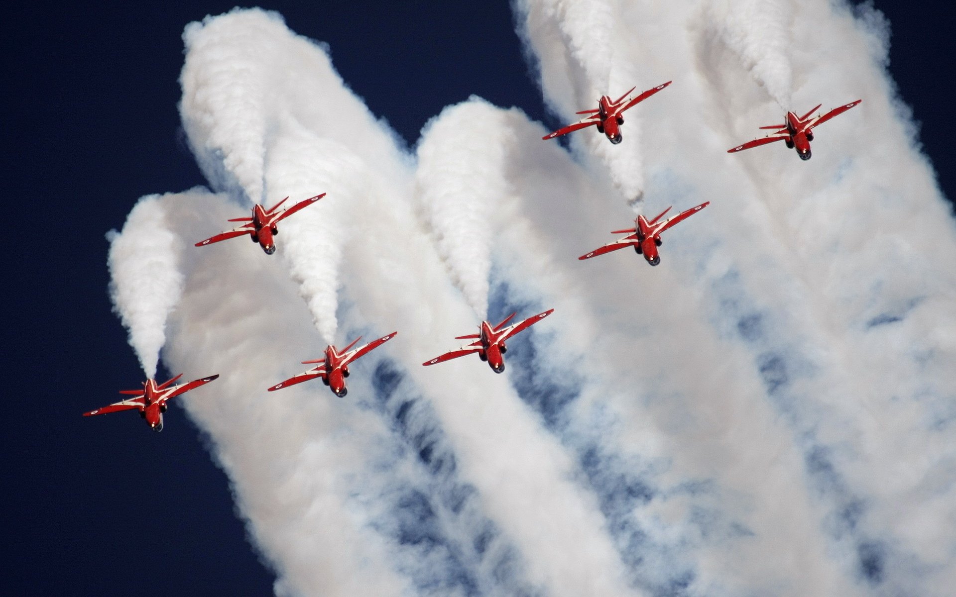 HD desktop wallpaper featuring a military air show with red jets performing synchronized maneuvers, leaving trails of white smoke against a clear blue sky.
