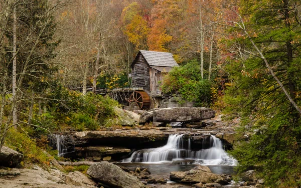 HD desktop wallpaper featuring a man-made watermill beside a flowing stream surrounded by autumn foliage in a serene natural setting.
