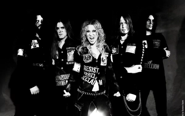 Black-and-white 2K Quad HD PC desktop wallpaper of a metal music band posing, fierce female lead singer center with intense expression, bandmates flanking her in leather and studs.