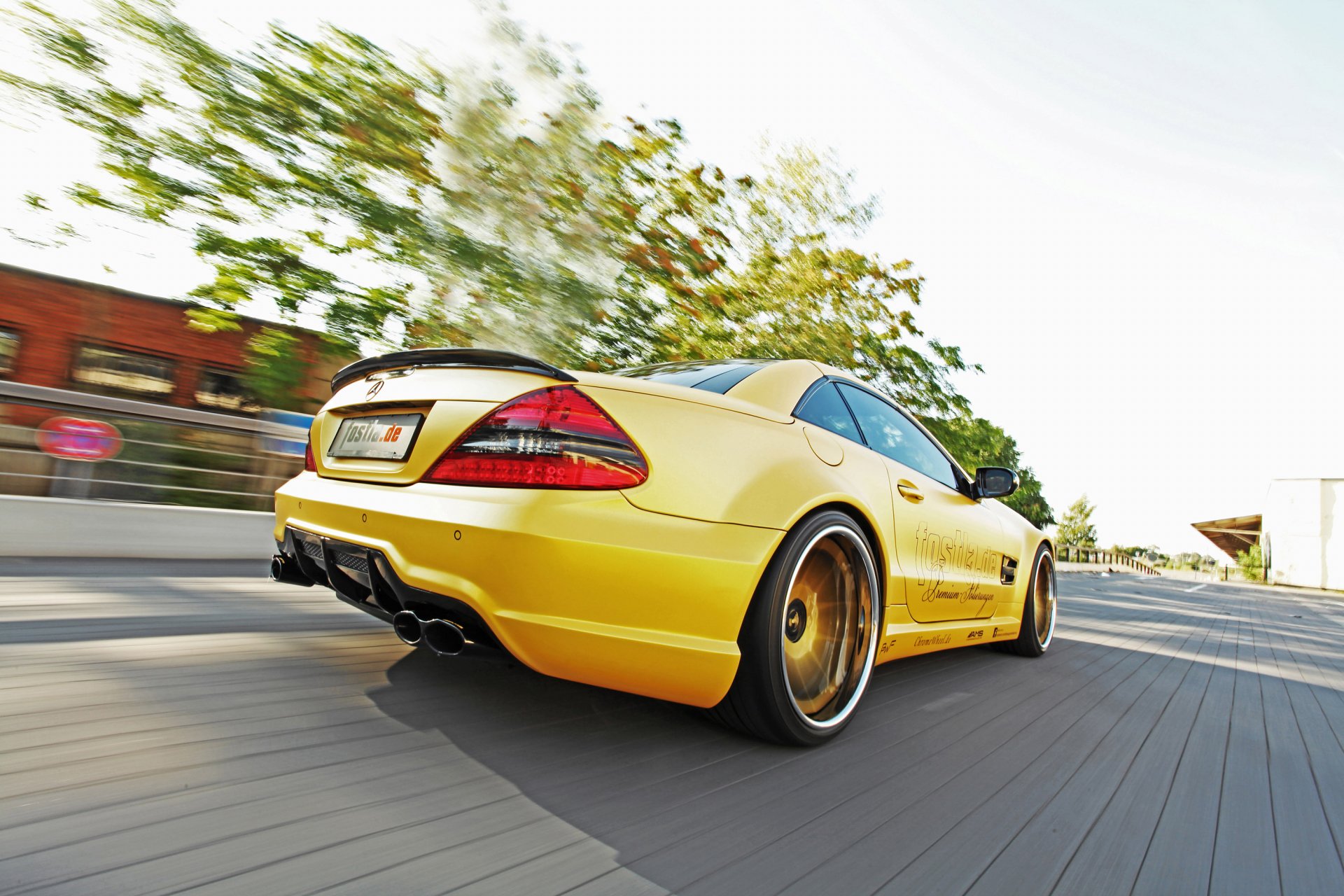 Yellow Mercedes-Benz SL 55 AMG captured in motion on a sunlit road, featured as a high-definition PC desktop wallpaper.