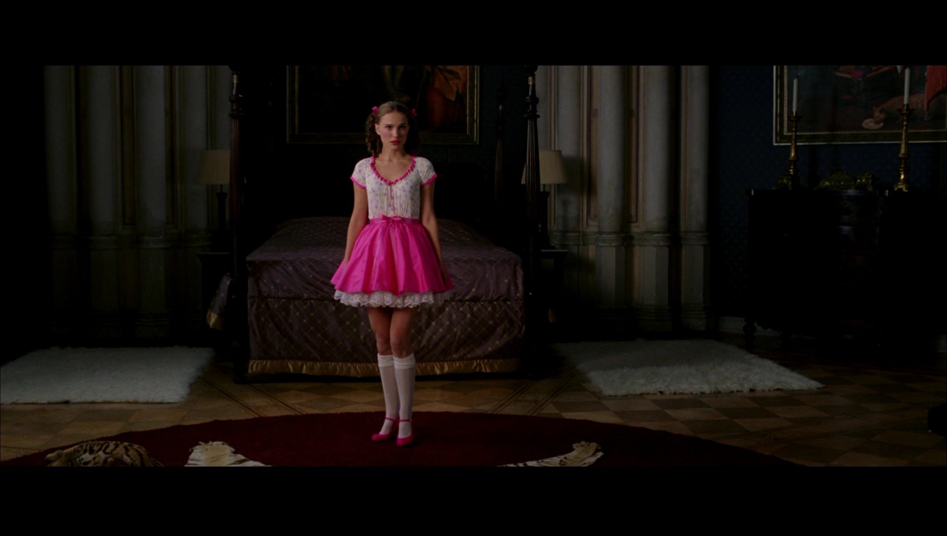 HD PC desktop wallpaper/background: scene from the movie V for Vendetta — a girl in a bright pink dress and red shoes stands centered in a dim, cathedral-like bedroom with a large bed behind her.