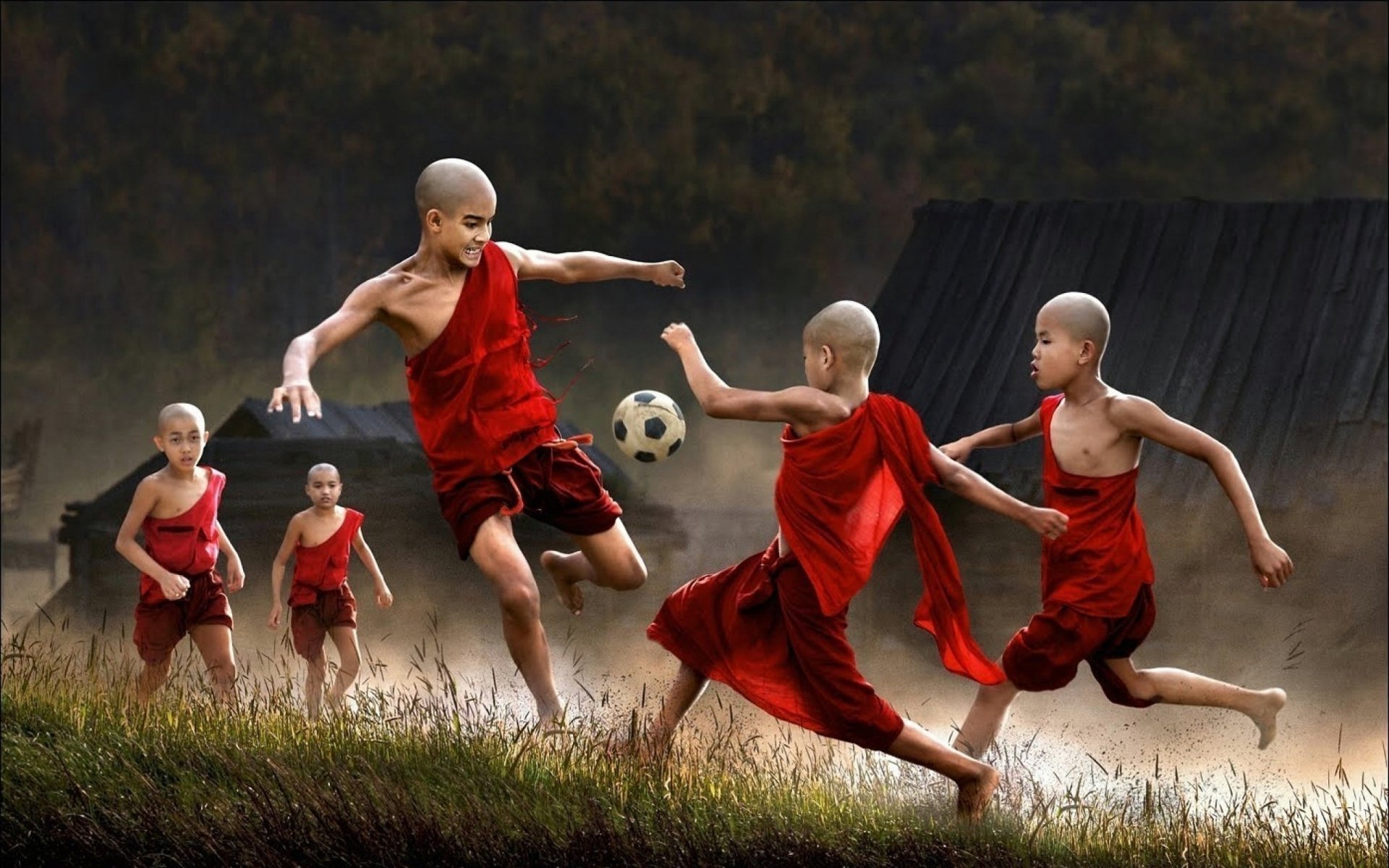A vibrant HD desktop wallpaper depicting young monks in red robes energetically playing soccer, capturing the excitement and spirit of sports in a serene outdoor setting.