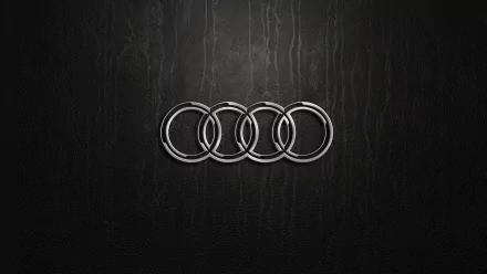 A sleek HD wallpaper featuring the Audi logo prominently displayed against a textured black background, showcasing the brand’s iconic four rings.