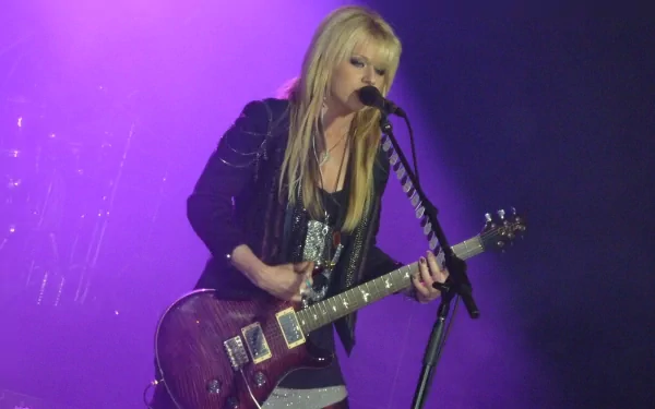 HD PC desktop wallpaper featuring musician Orianthi passionately playing electric guitar and singing on stage under purple lighting.