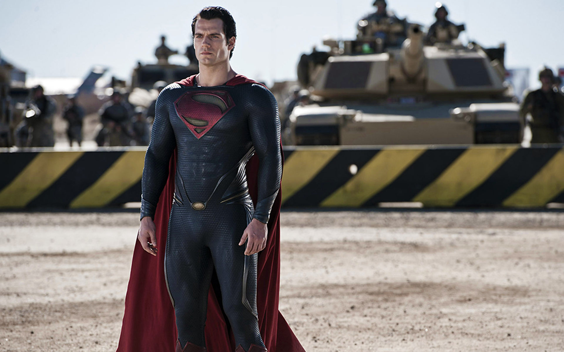 Henry Cavill as Superman in the Man of Steel movie stands confidently in front of military tanks in this HD PC desktop wallpaper.