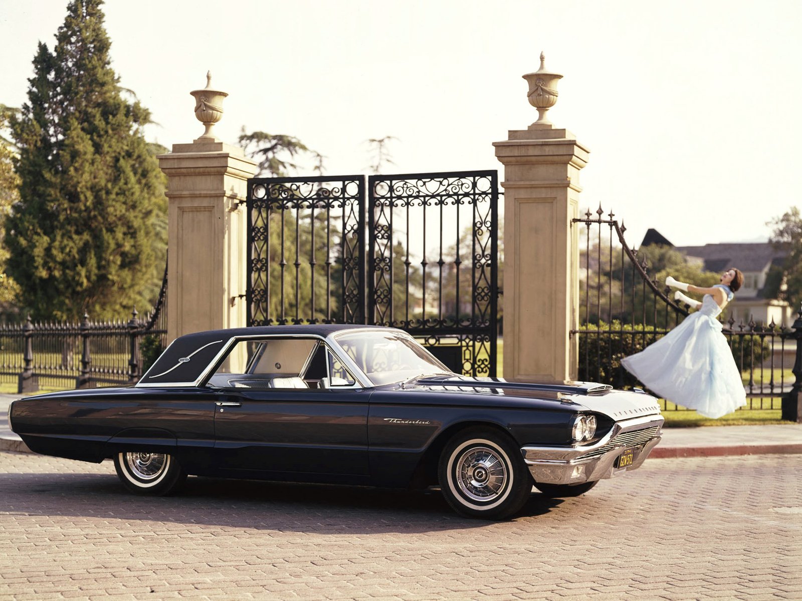 1964 Ford Thunderbird Landau Coupe parked in front of ornate gates with a bride twirling in the background, captured in HD for a PC desktop wallpaper.