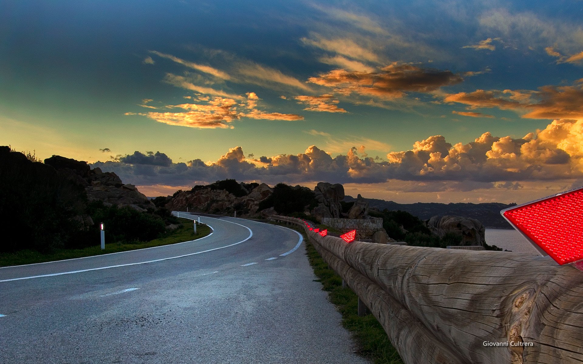 HD PC desktop wallpaper of a man-made winding road along a stone barrier, sweeping toward a horizon of dramatic golden sunset clouds.