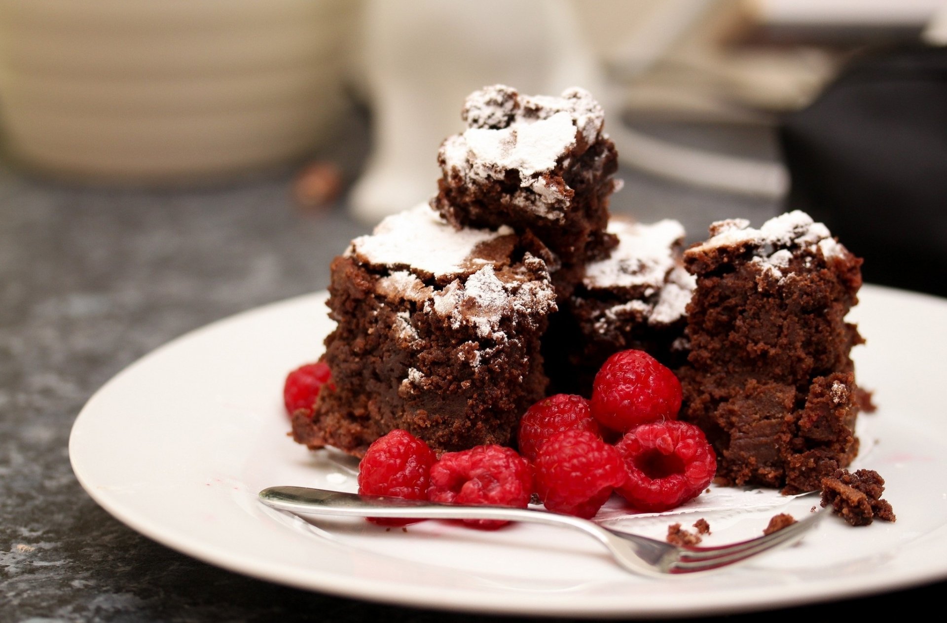 A tempting plate of chocolate cake pieces dusted with powdered sugar, garnished with fresh raspberries, serves as an inviting HD desktop wallpaper.