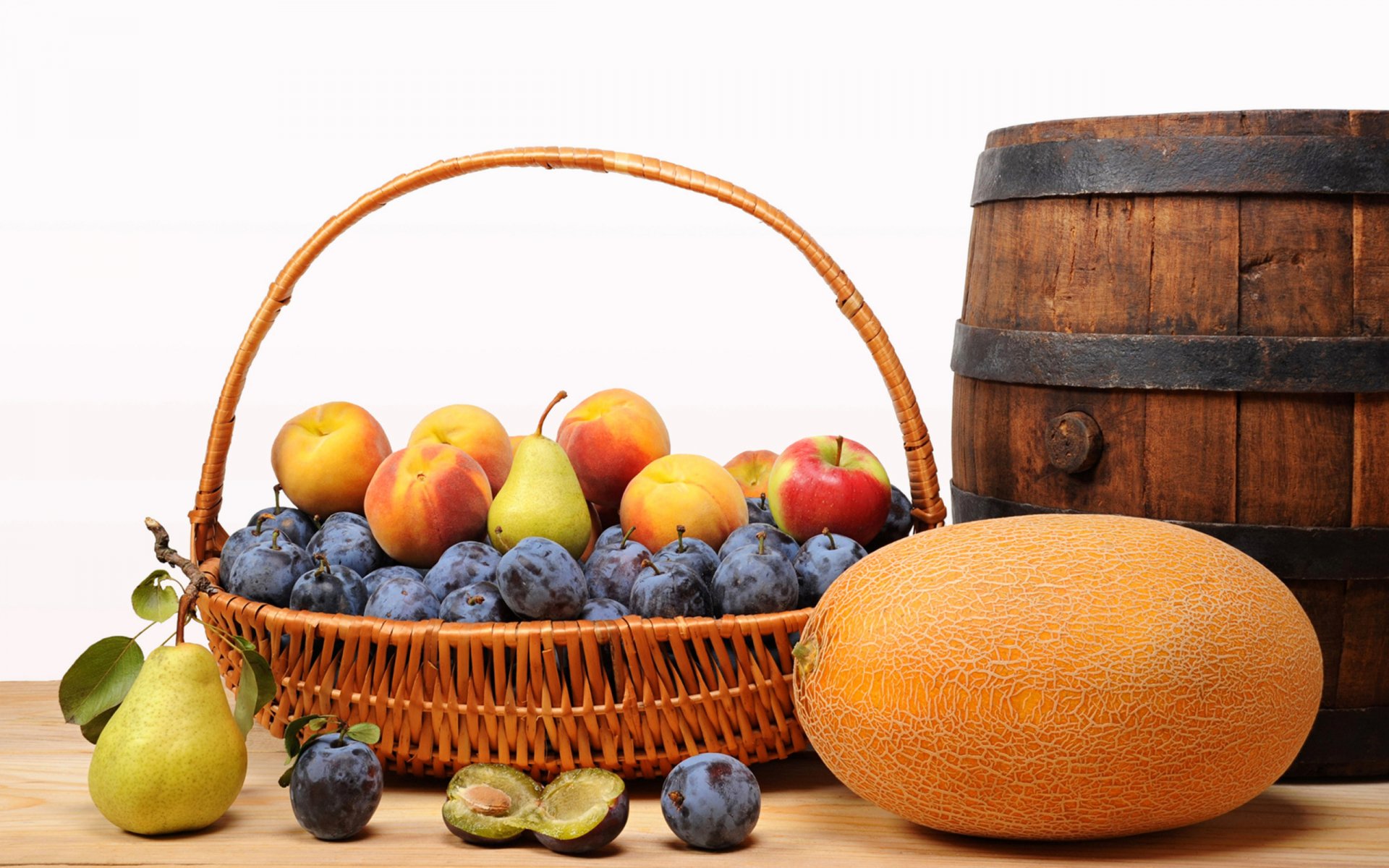 HD PC desktop wallpaper featuring a basket of assorted fresh fruits, including peaches, plums, pears, and an orange melon, alongside a rustic wooden barrel.