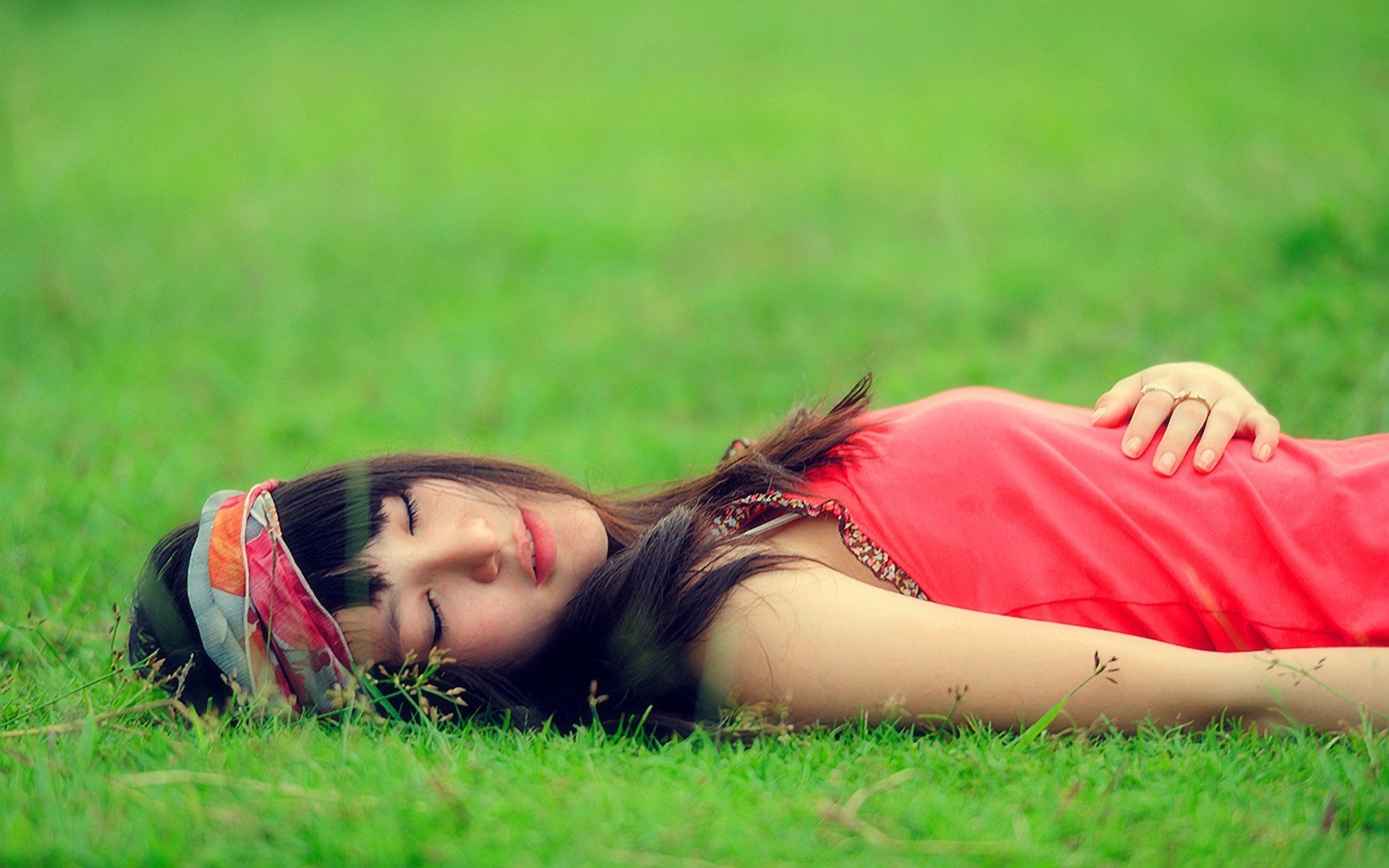 A woman in a vibrant outfit lies peacefully on green grass, embodying a serene mood. This high-definition image serves as a calming desktop wallpaper and background.
