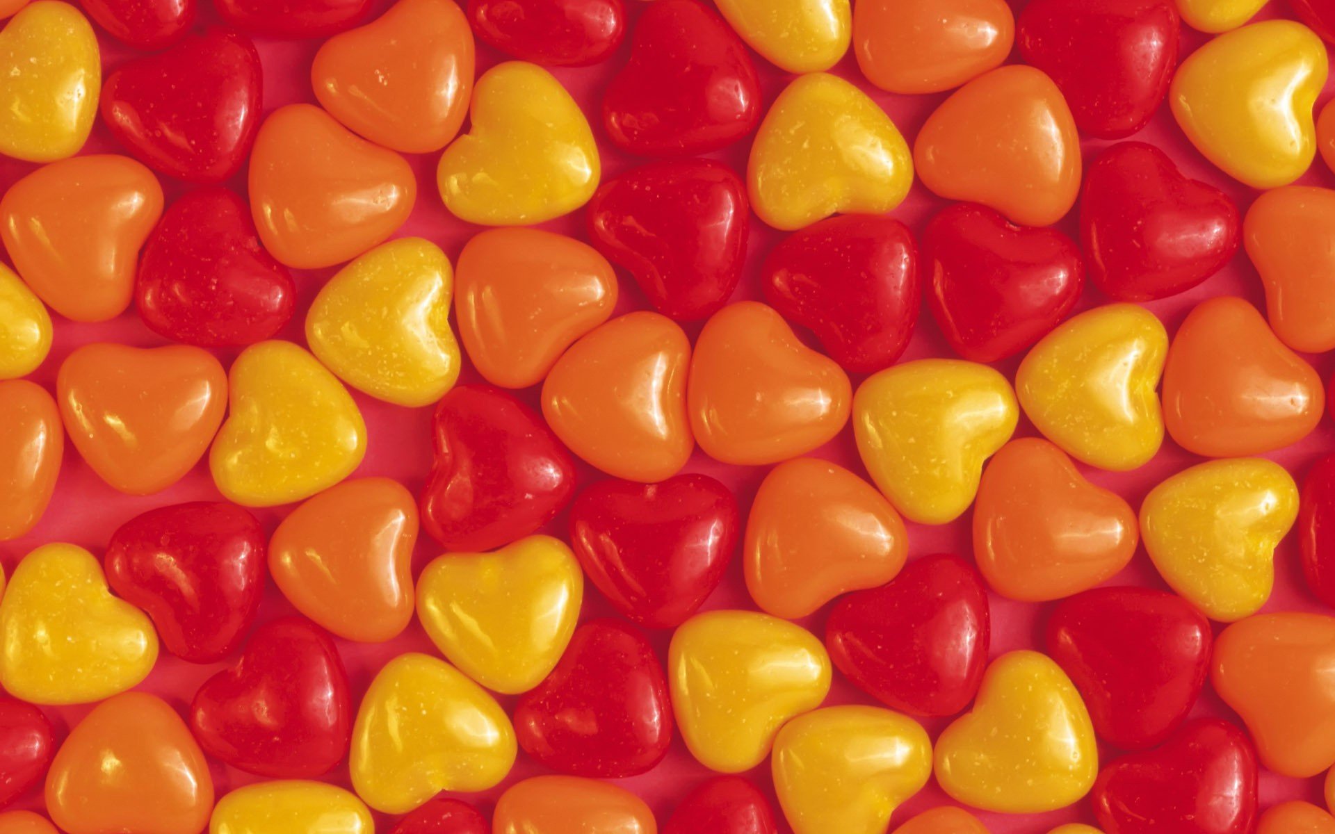 Artistic HD PC desktop wallpaper featuring a vibrant pattern of glossy red, orange, and yellow heart shapes against a red textured background.