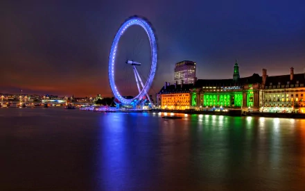 HD desktop wallpaper showing the illuminated London Eye and surrounding buildings at night, reflecting on the Thames River in London.