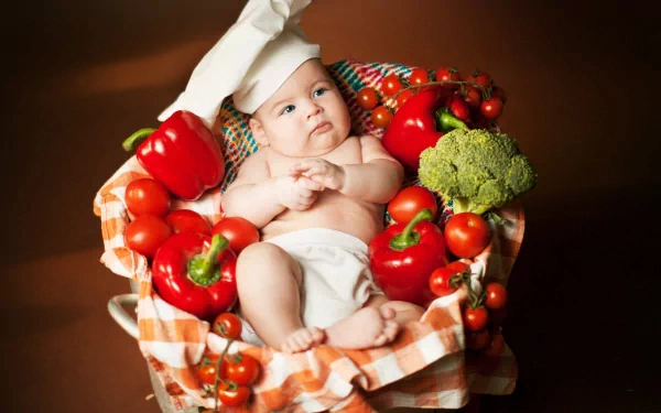 4K Ultra HD photography of a baby wearing a chef hat, surrounded by fresh vegetables like tomatoes, broccoli, and bell peppers on a checkered cloth.