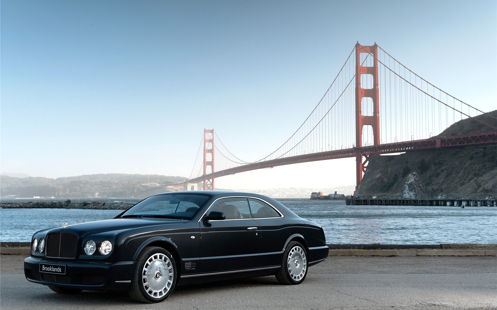 HD PC desktop wallpaper of a black Bentley vehicle parked by the waterfront with the Golden Gate Bridge in the background.
