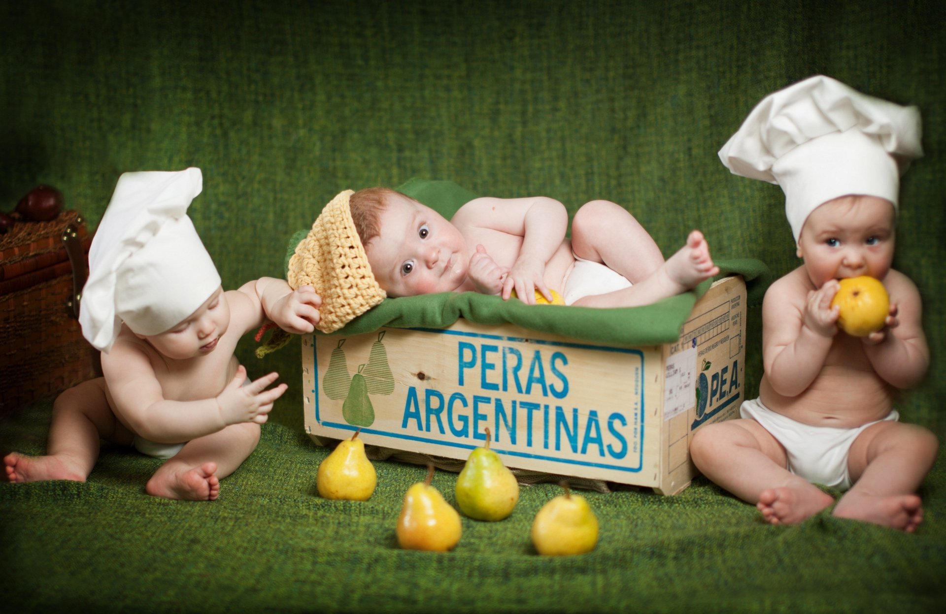 HD photography of three babies with chef hats playing around and inside a wooden crate labeled Peras Argentinas, set against a green backdrop for a PC desktop wallpaper.
