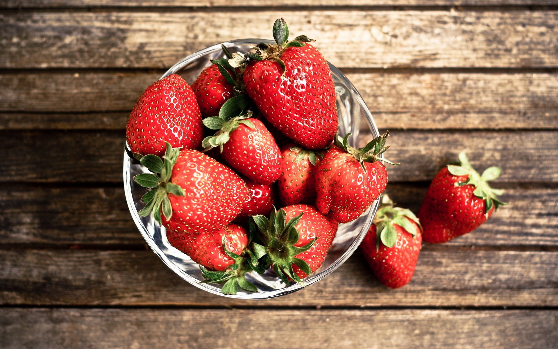 HD PC desktop wallpaper featuring fresh, vibrant strawberries in a glass bowl on a rustic wooden surface, highlighting bright red fruit and natural textures.