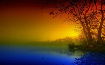 HD desktop wallpaper featuring a scenic nature view with a vibrant sunset casting warm orange and yellow hues over a calm body of water and silhouetted trees.