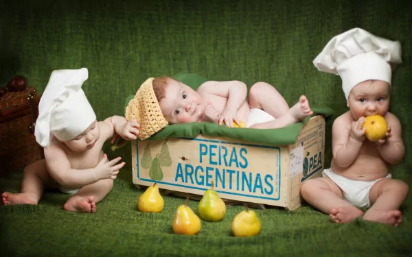 HD photography of three babies with chef hats playing around and inside a wooden crate labeled Peras Argentinas, set against a green backdrop for a PC desktop wallpaper.