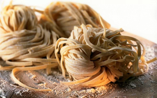 HD desktop wallpaper of fresh, uncooked pasta nests dusted with flour on a wooden surface, highlighting rustic food textures and natural lighting.