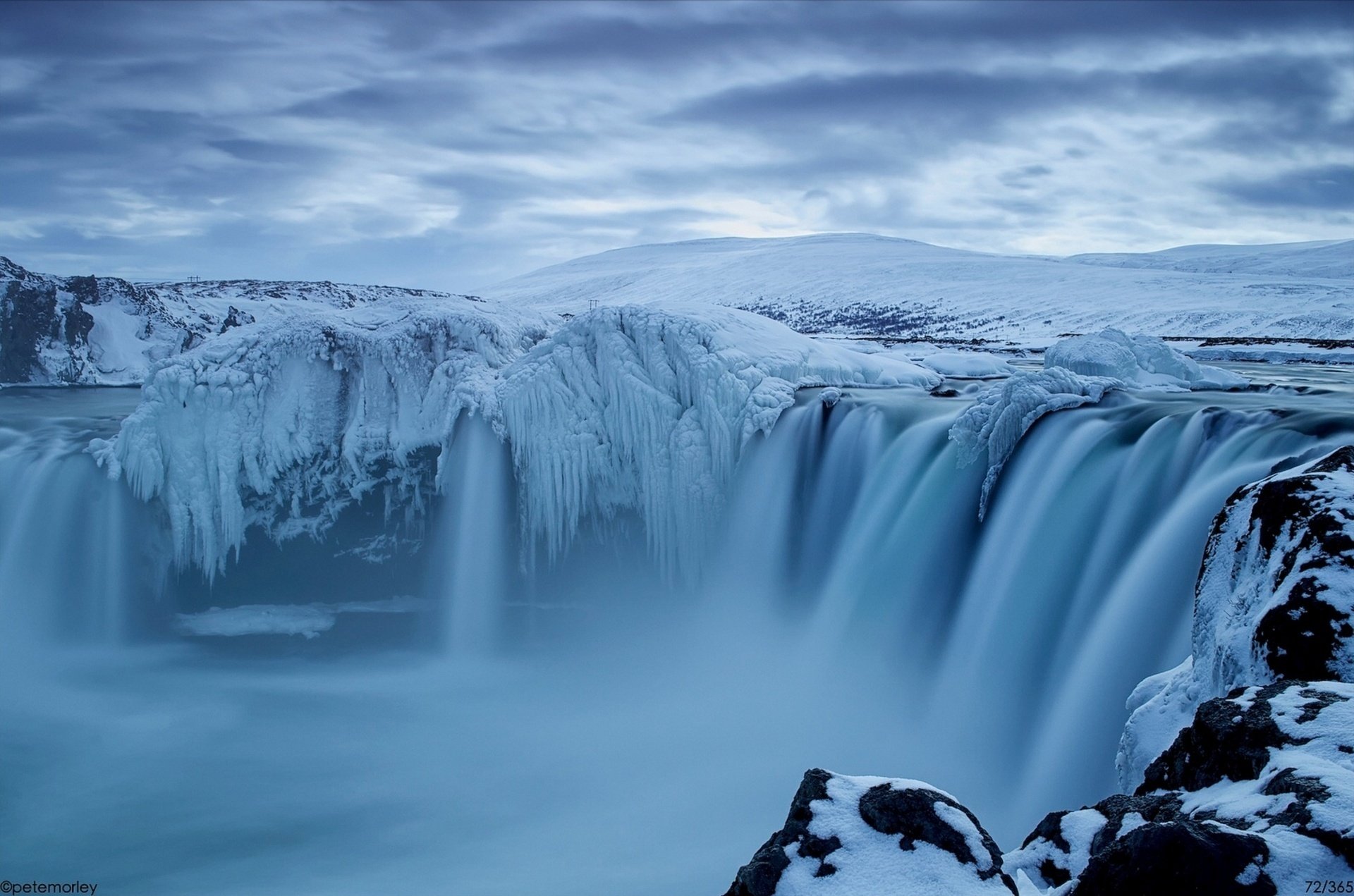 A breathtaking waterfall cascades over icy cliffs, surrounded by a serene winter landscape, showcasing the beauty of nature in this HD desktop wallpaper.