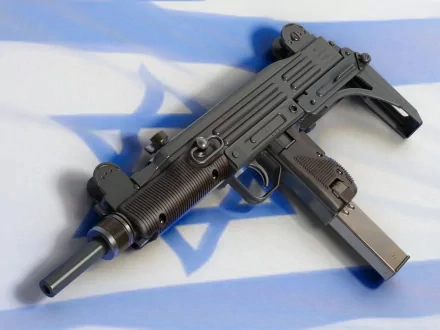 HD desktop wallpaper featuring a close-up of a man-made Uzi submachine gun resting on a surface with a blue and white background.