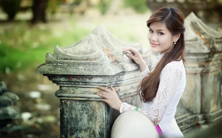 A woman stands beside an ancient stone structure, wearing a white dress, in an HD desktop wallpaper and background. The serene scene features greenery in the backdrop.