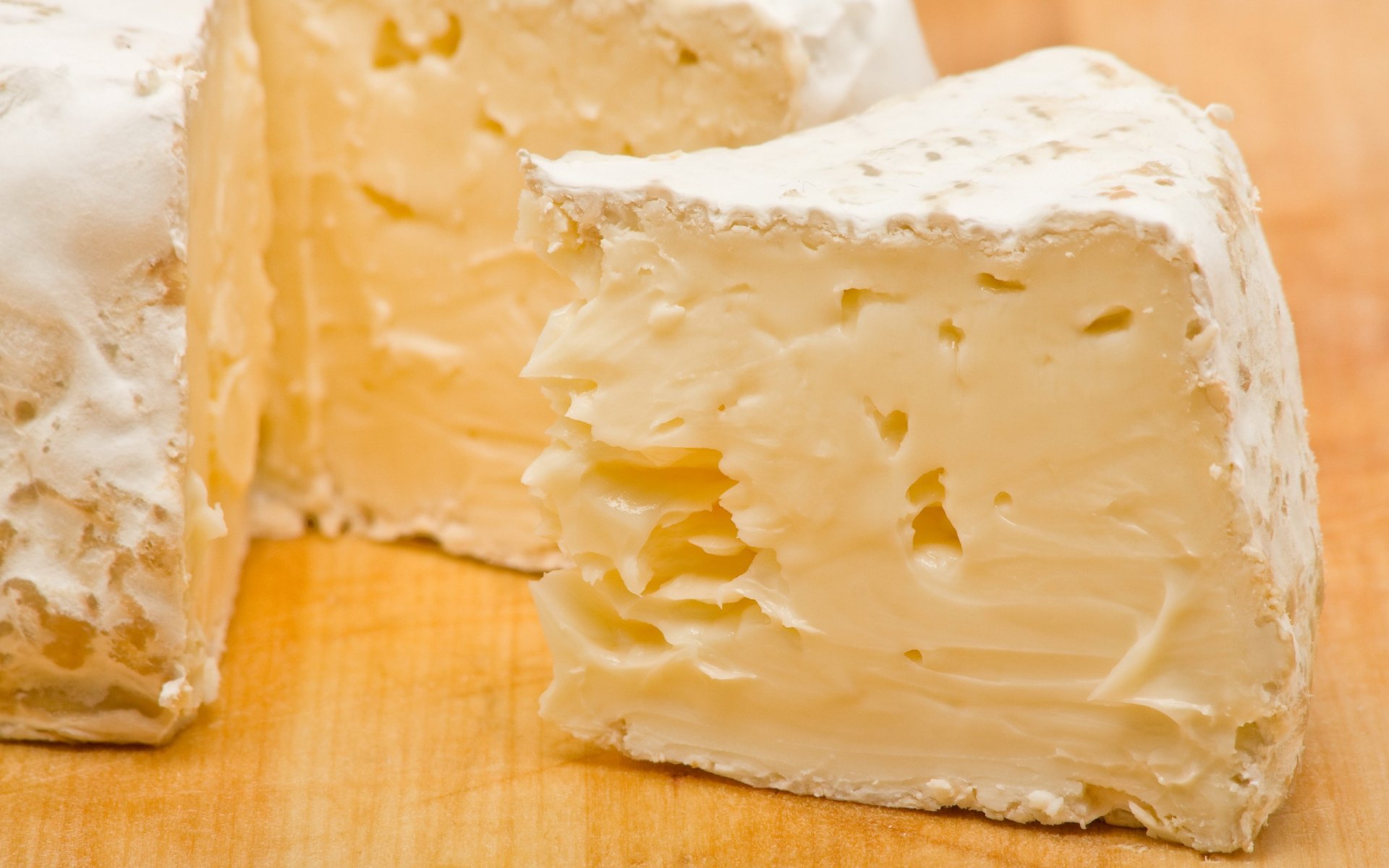 Close-up HD desktop wallpaper of creamy soft cheese with a white rind, showcasing its smooth texture on a wooden surface.