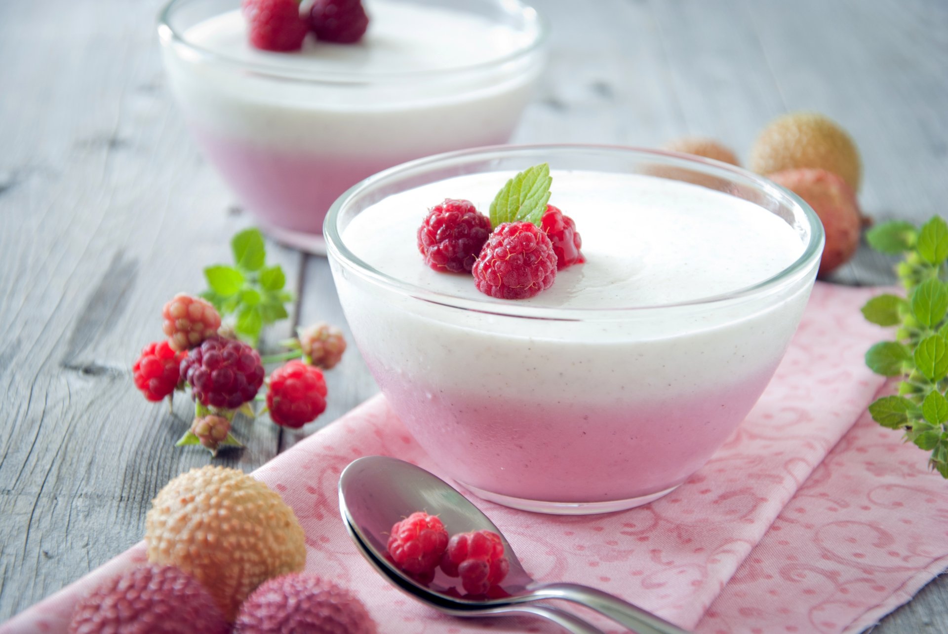 HD desktop wallpaper featuring a delicious dessert of layered pink and white mousse in glass bowls, garnished with fresh raspberries and mint, with spoons and additional raspberries on a wooden surface.
